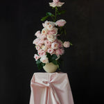 Pale garden roses in a cream vessel on pink silk