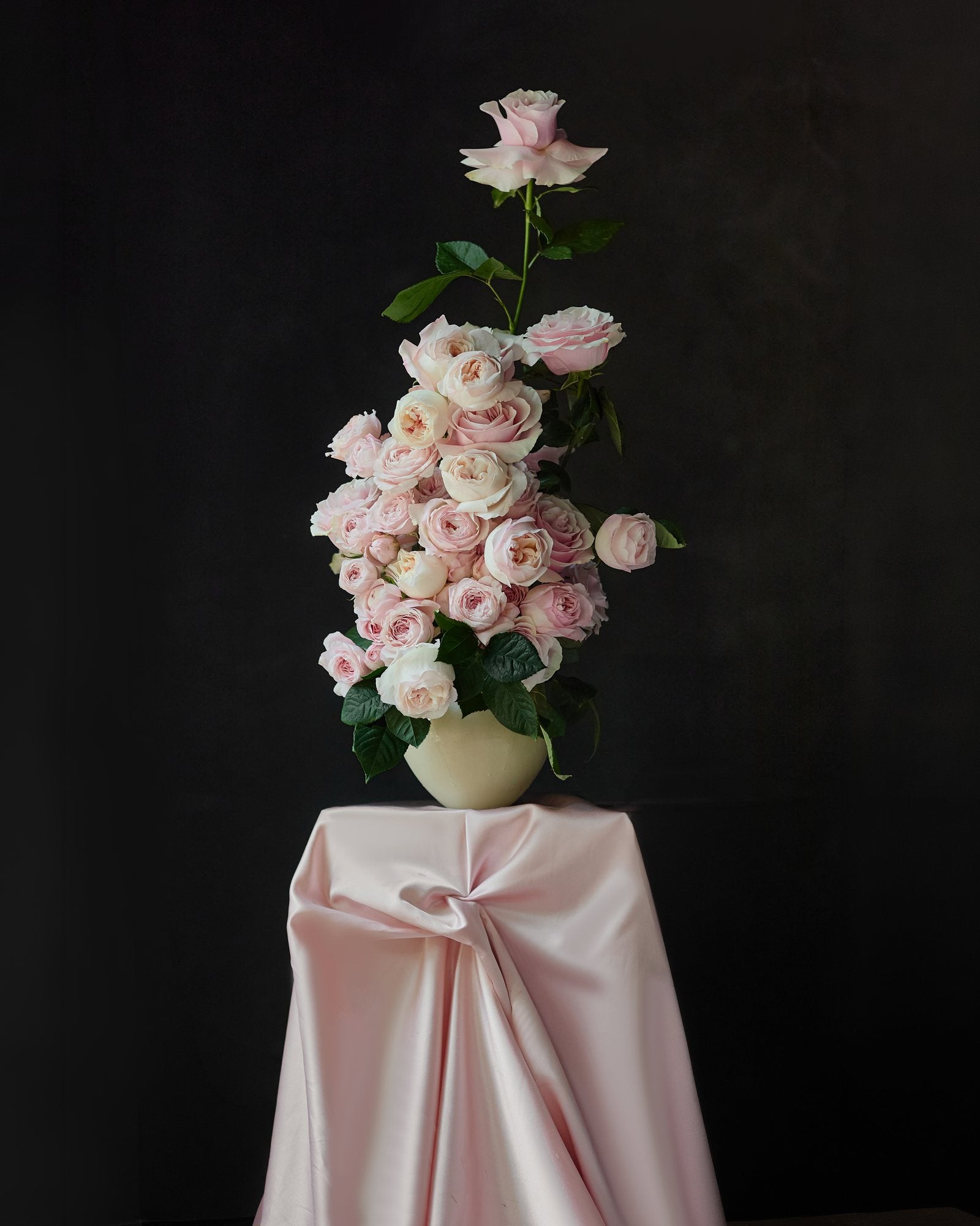 Pale garden roses in a cream vessel on pink silk